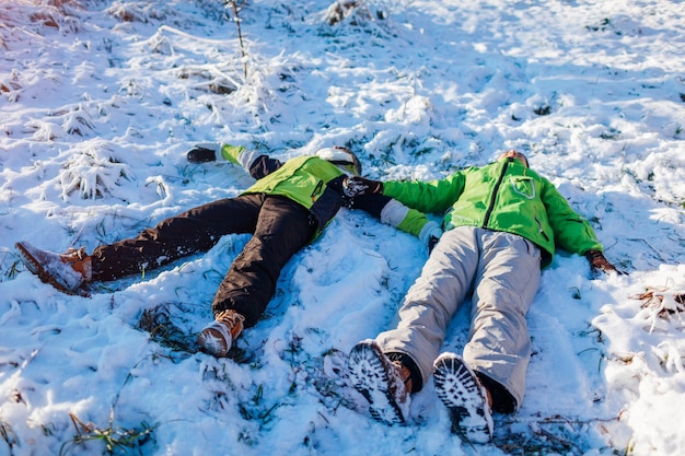 Молодая влюбленная пара лежит в снегу и делает снежных ангелов, люди веселятся в зимнем лесу