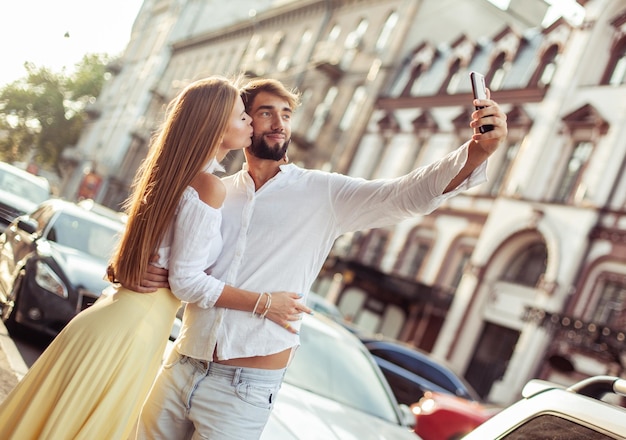 若い恋人カップルは街でスマートフォンでセルフィーを撮りますロマンチックな愛のコンセプト