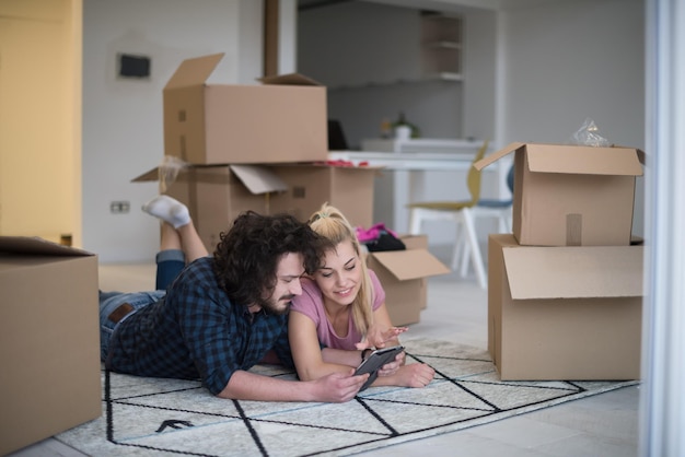 Young couple in love moving in a new flat, lying on the floor and surfing the web on a tablet computer in search of new redecoration ideas