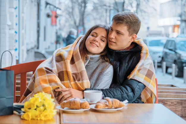 Young couple in love in outdoor cafe under plaid