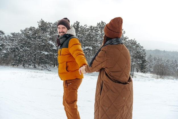 雪に覆われた冬の森の屋外で恋をしている若いカップル