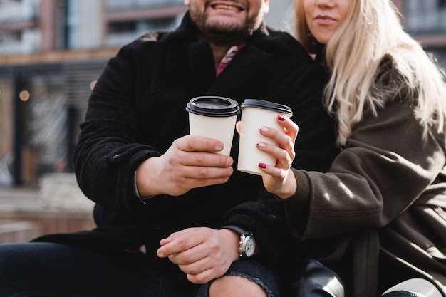 Giovani coppie nell'amore all'aperto. i viaggiatori con tazze di caffè stanno camminando nel parco di primavera. bella giornata di sole. una giovane coppia che beve caffè per andare