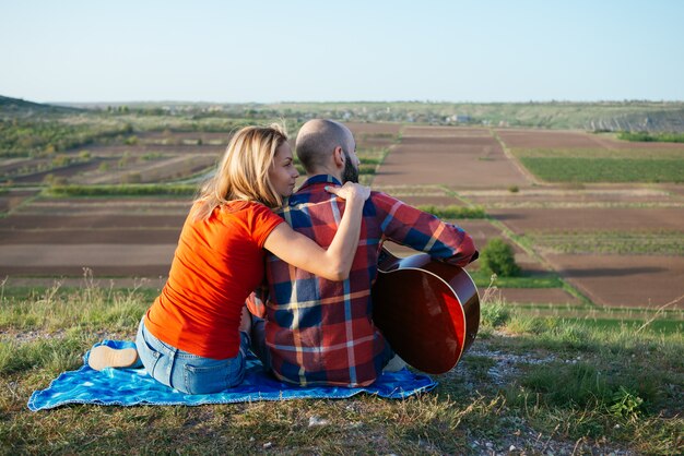 Foto giovani coppie nell'amore che si siede sul parco mentre queste giovani chitarre che suonano la chitarra nel tempo del tramonto.