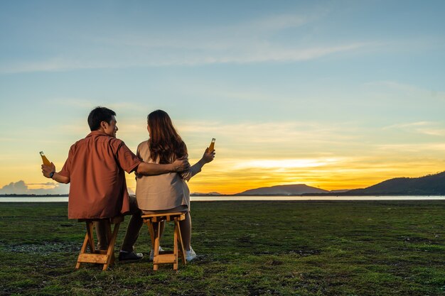 Young couple in love sitting and party at the grass filed at sunset