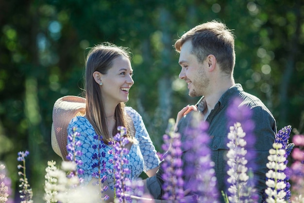 Young couple in love smile and hug in nature in flowers Beautiful park with blooming purple lupins Love and tenderness