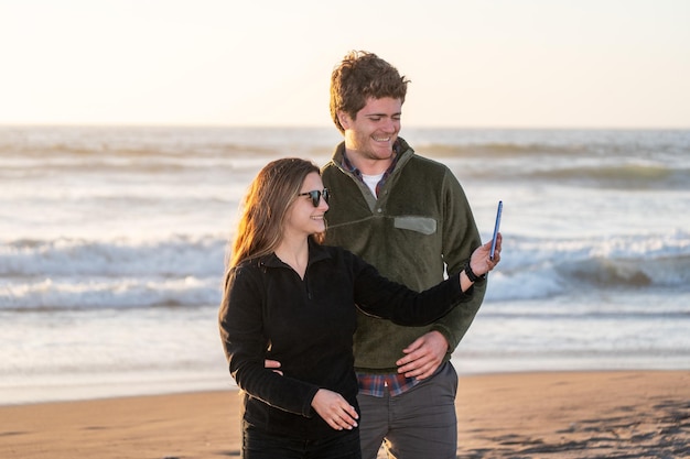 young couple in love taking selfies on the beach at sunset