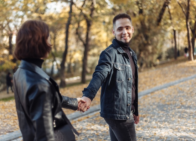 Young couple in love walking in the autumn city park holding hands. Romantic date