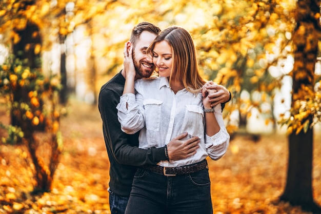 A young couple in love walking in the autumn park on a sunny day. The man gently hugs the woman. Love story