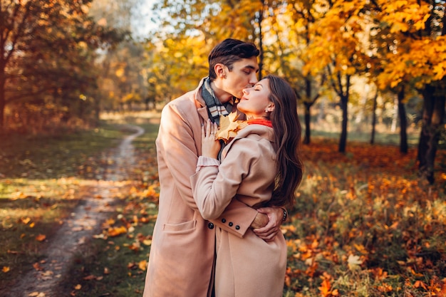 Влюбленная молодая пара гуляет в осеннем лесу среди красочных деревьев. Люди обнимаются и целуются