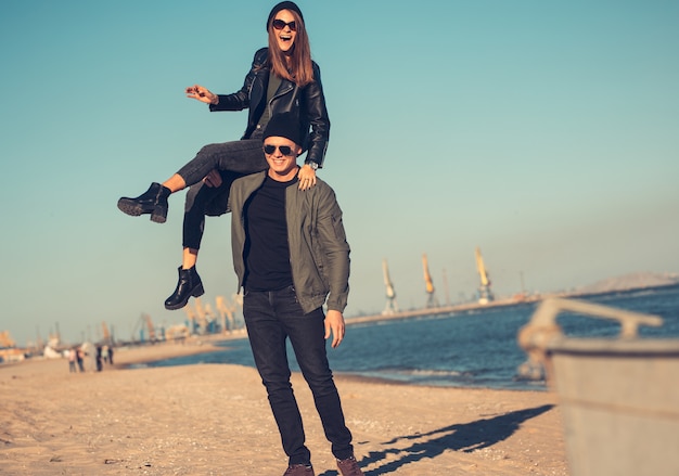 Young couple in love walks by the sea. Spring, autumn. The guy is wearing a jacket and hat. Girl in a hat and leather jacket with a scarf and glasses