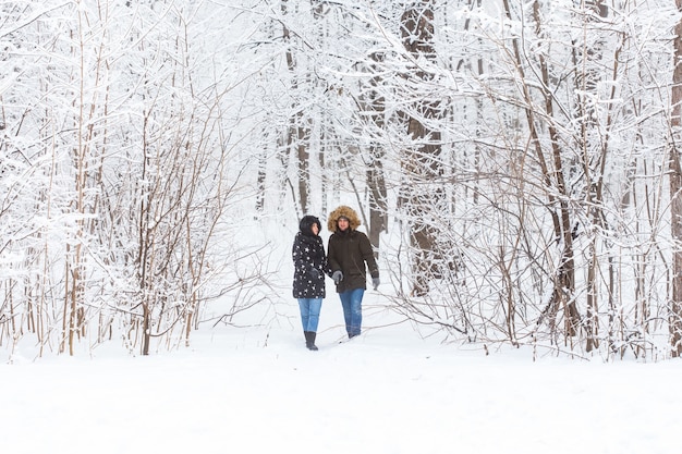 사랑에 빠진 젊은 부부는 눈 덮인 숲에서 활동적인 겨울 휴가를 걷습니다.