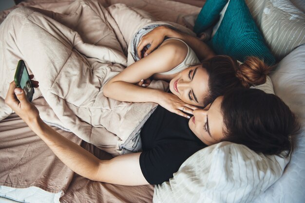 Young couple lying in bed and embracing while smile and making selfie covered with a quilt early morning