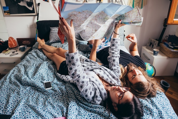 사진 여행 계획을 읽고 침대 계획에 누워있는 젊은 부부