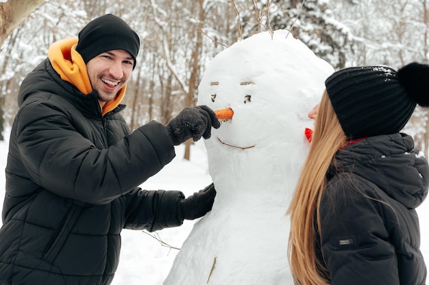 若いカップルが雪の公園で雪だるまを作った