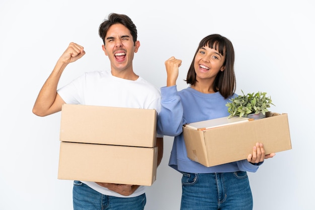 Young couple making a move while picking up a box full of things isolated on white background celebrating a victory