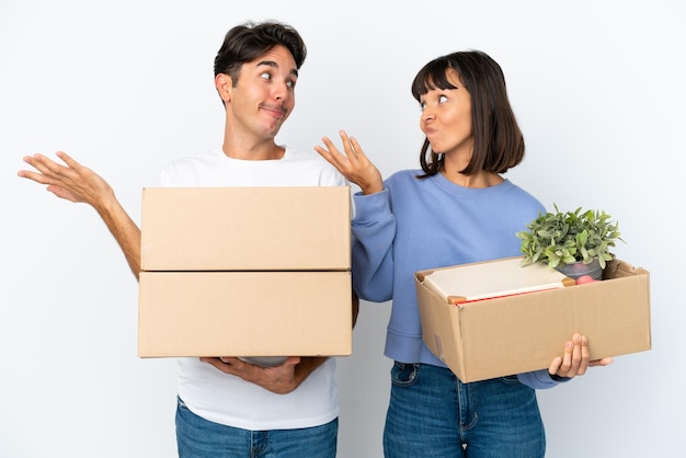 Young couple making a move while picking up a box full of things isolated on white background making unimportant gesture while lifting the shoulders