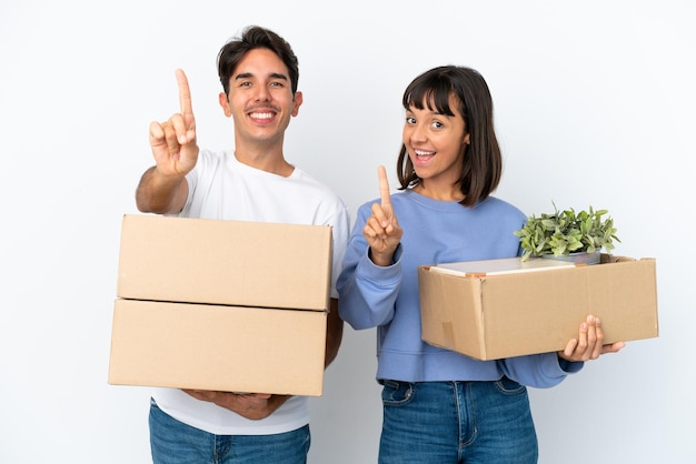 Young couple making a move while picking up a box full of things isolated on white background showing and lifting a finger