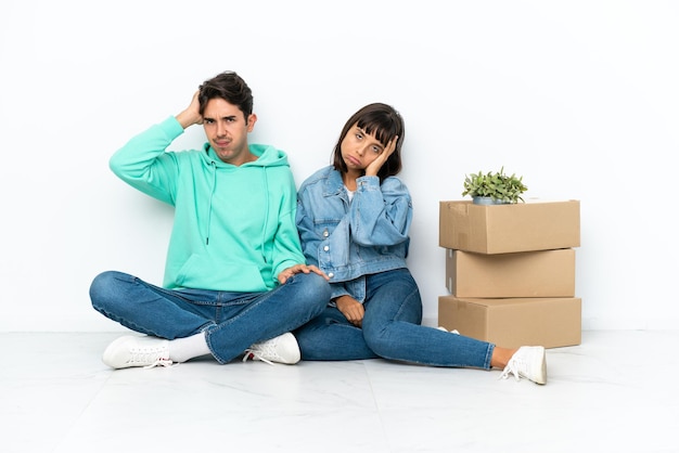 Young couple making a move while picking up a box full of things sitting on the floor isolated on white background with an expression of frustration and not understanding