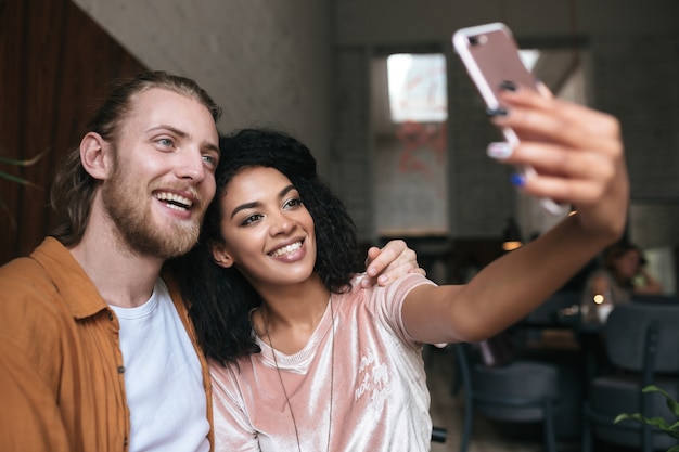 Young couple making photos on frontal cellphone camera in restaurant