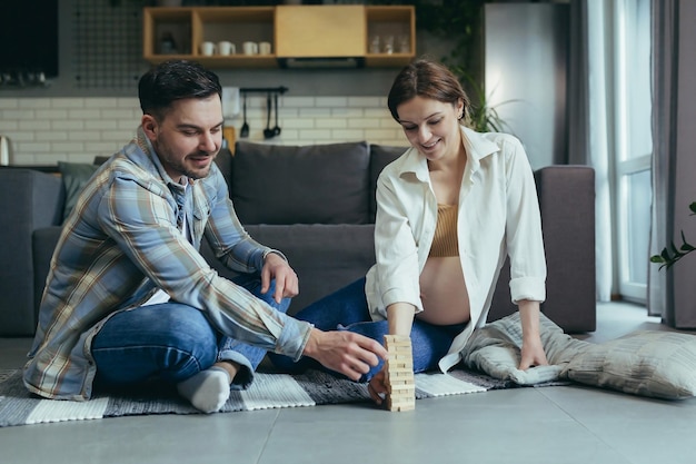 Young couple man and pregnant woman playing board game of jang together sitting on the floor at home having fun together