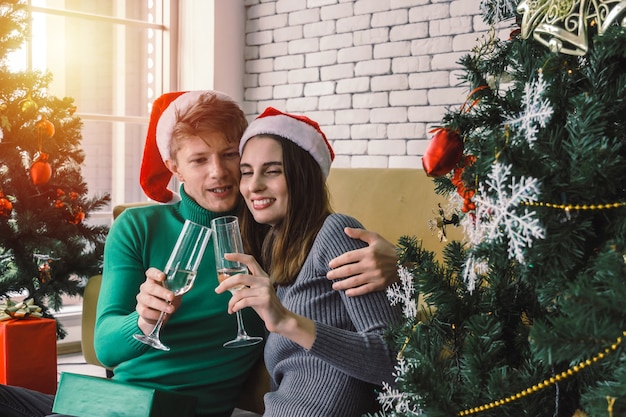 Young couple man with red santa hat enjoy drinking champagne with girlfriend with christmas tree celebrating in house, christmas holiday family, happy new year and merry christmas festival concept