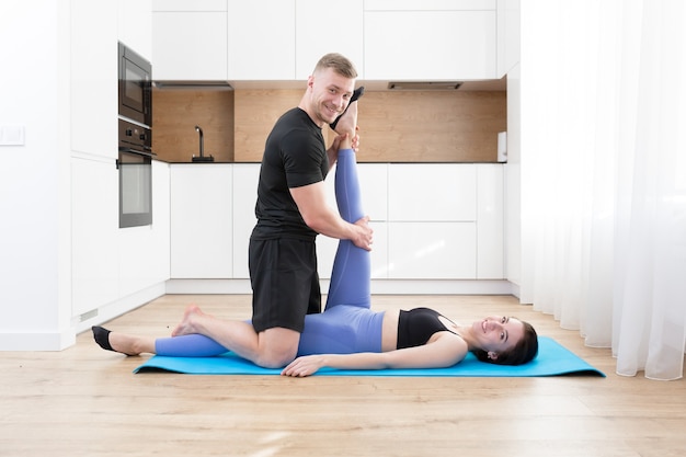 young couple man and woman doing fitness together at home on the floor, two people doing sports exercises in the kitchen on a sports mat