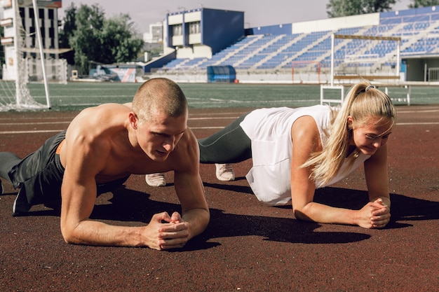 スタジアムの腹筋と皮質トレーニングで板の運動をしている若いカップルの男性と女性