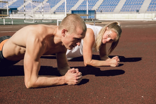 スタジアムの腹筋と皮質トレーニングで板の運動をしている若いカップルの男性と女性