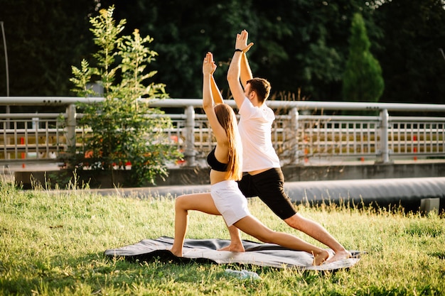 Young couple man and woman doing sports, yoga on city lawn, summer evening, stretching together on sunset, city lifestyle