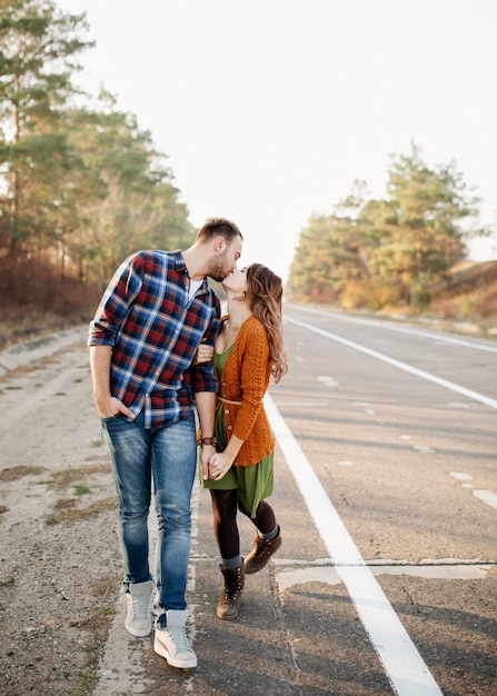 男と女の若いカップルがキスをし、空の道を屋外で歩いています。