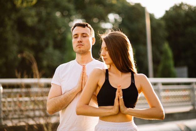 Young couple man and woman meditate while standing, yoga on city lawn, summer evening, lifestyle