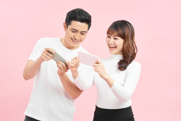 young couple man and woman peeking at each others cell phones holding in hands isolated over pink background