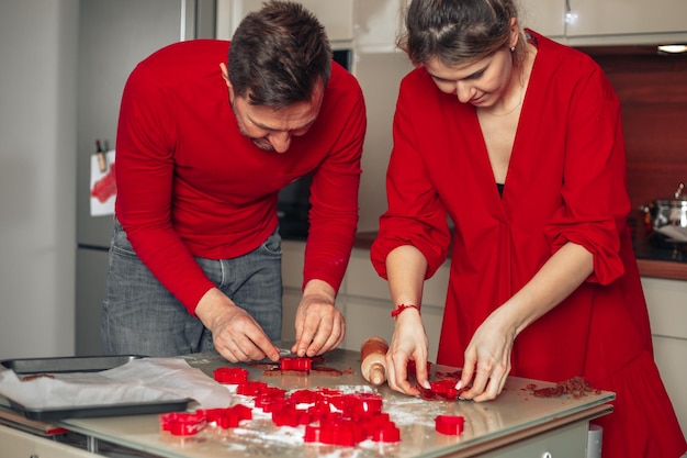 Молодая пара, мужчина и женщина готовят рождественское печенье на уютной кухне. Используйте формы для вырезания печенья. Счастливые моменты. Красные цвета, работа в команде. 40 лет