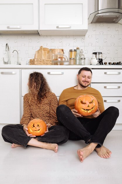 Photo young couple man and woman sitting on the floor at kitchen at home having fun and preparing for halloween talking laughing cheerful.