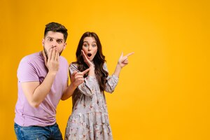 Young couple man and woman surprised pointing at copyspace