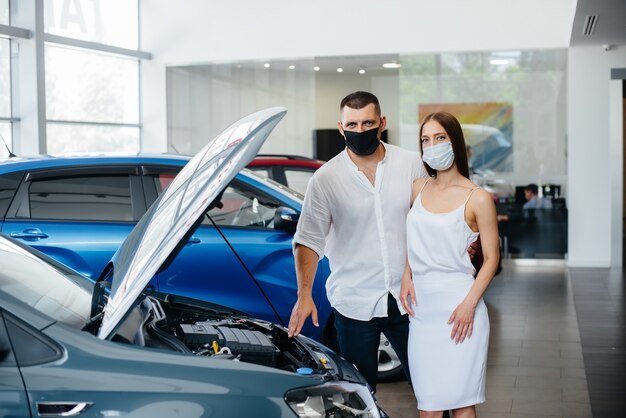 Young couple in masks selects a new vehicle and consult with a representative of the dealership in the period of the pandemic. Car sales, and life during the pandemic.