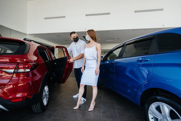 Young couple in masks selects a new vehicle and consult with a representative of the dealership in the period of the pandemic.