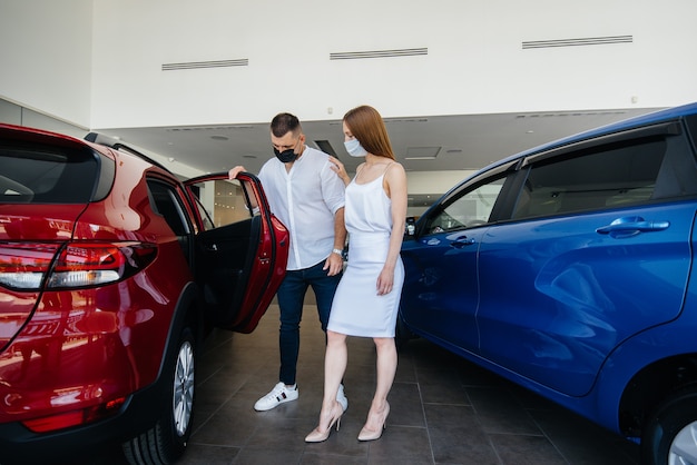 Young couple in masks selects a new vehicle and consult with a representative of the dealership in the period of the pandemic.