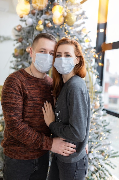 크리스마스 트리 근처 의료용 마스크를 쓴 젊은 부부. 전염성 아픈 사람