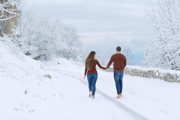 若いカップルの男性と女性が白い雪に覆われた道を歩いています