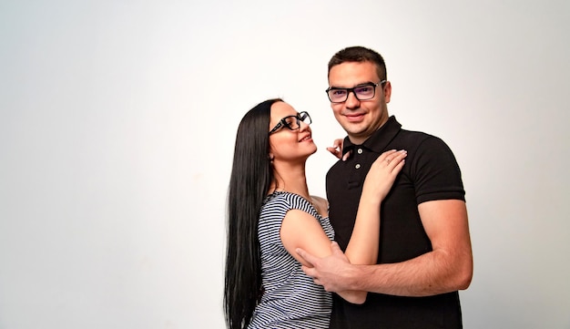 Young couple in modern spectacles hug each other blurred grey\
background boy and a girl in eyeglasses longhaired brunette\
beautiful woman and handsome man