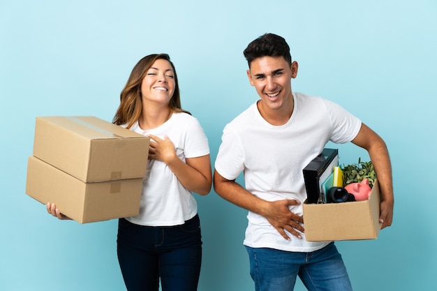 Young couple moving in new home among boxes on blue smiling a lot while putting hands on chest