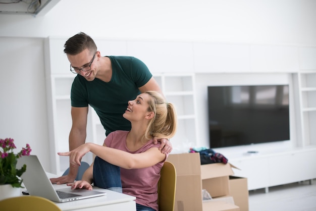 Photo young couple moving in a new home. man and woman at the table using notebook laptop computer and plans with boxes around them