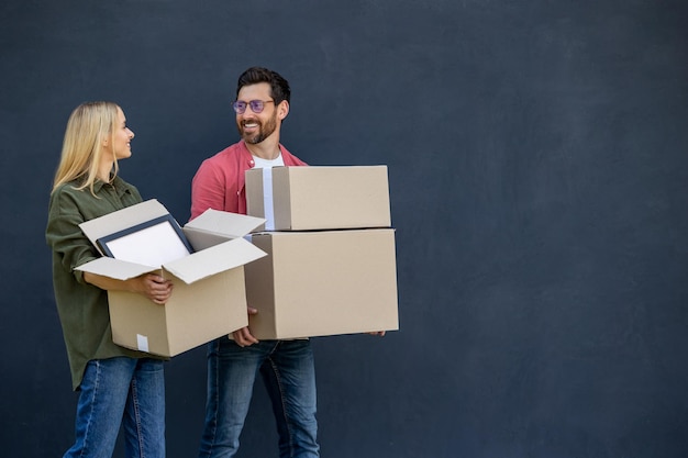 Young couple moving to a new house and carrying boxes with clothes