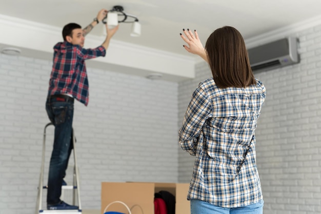 Young couple moving in new house changing a light bulb