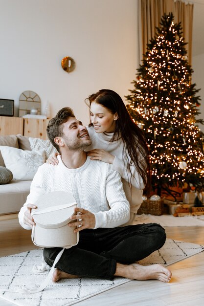 クリスマスツリーの前のリビングルームでクリスマスプレゼントを開く若いカップル