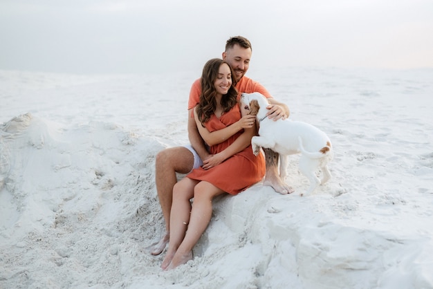 Young couple in orange clothes with dog in the desert white sands