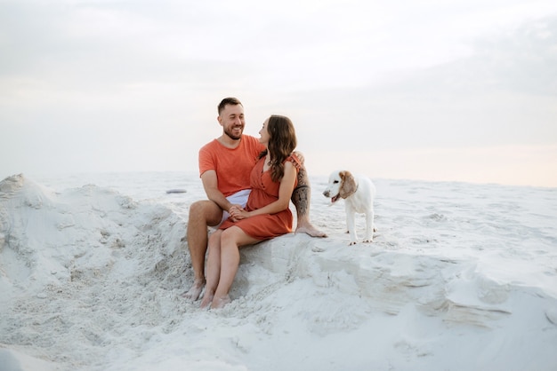 Young couple in orange clothes with dog in the desert white sands