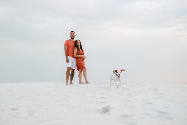 Young couple in orange clothes with dog in the desert white sands