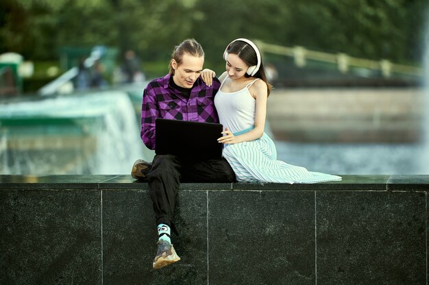 Young couple on an outdoor date uses laptop computer to listen to music through wireless headphones